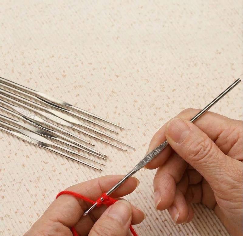 detailed view of a metal crochet hook and red yarn being used for precise hand-stitched patterns