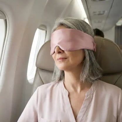 senior female traveler wearing a pink silk sleep mask for a restful nap during an airplane flight